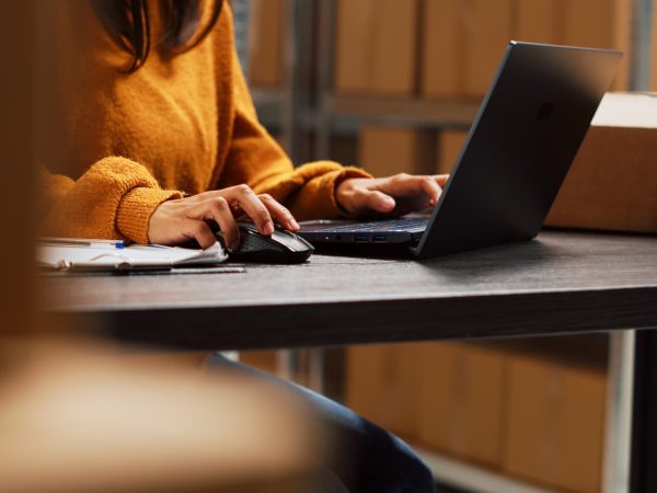 Startup owner working on stock inventory with laptop, planning order distribution for business management in storage room. Worker doing supply chain shipment at desk, retail products. Handheld shot.